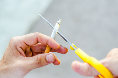 Cropped hands of man cutting cigarette with scissors 