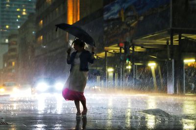 Woman under umbrella standing on street during rainfall