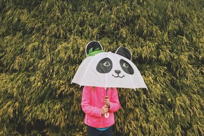 Girl holding umbrella standing against trees