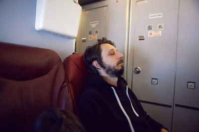 Man in a black jacket with a hood slip is a passenger of the plane sitting on a chair