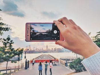 Cropped image of hand holding camera against sky