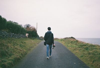 Rear view of man walking on road against sky