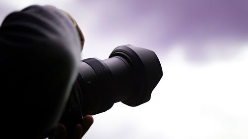 Close-up of person photographing camera against sky