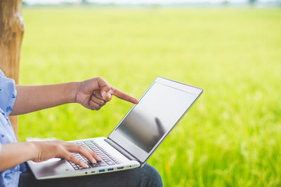 Midsection of woman using laptop while sitting against plants