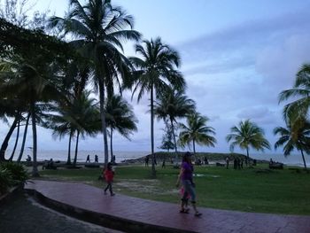 People walking by palm trees on beach against sky