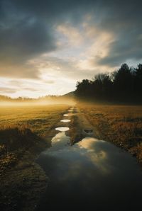 Puddle on dirt road against sky at morning