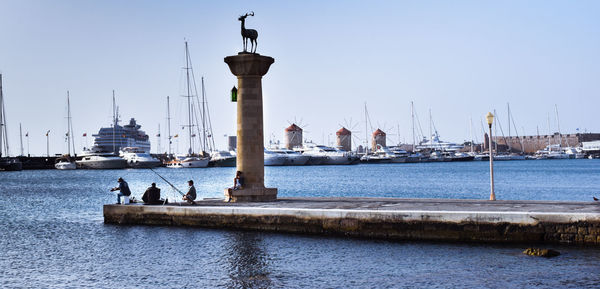 Sailboats on harbor by sea against sky