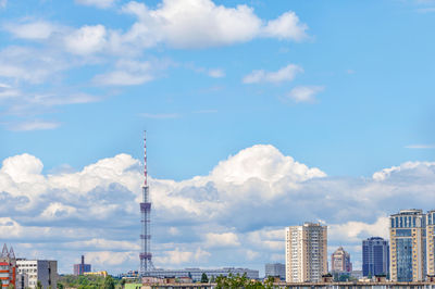 A tall tv tower against a blue sky in an urban summer landscape.