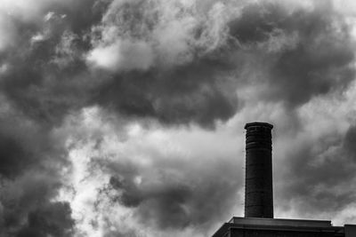 Low angle view of smoke stacks against cloudy sky