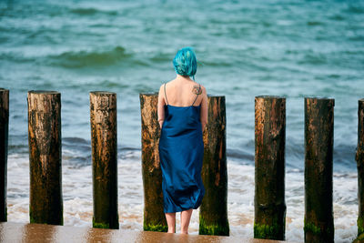 Rear view of woman standing by wooden post in sea