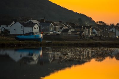 Houses by lake against sky during sunset