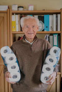 Portrait of smiling man holding toilet papers while standing at home