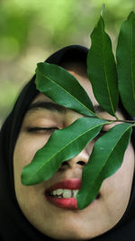 Close-up portrait of young woman with green leaves