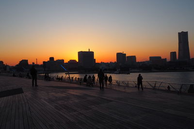 Silhouette people in city against clear sky during sunset