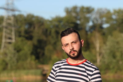 Portrait of young man standing against trees