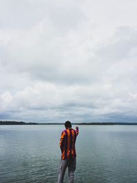 Rear view of man standing by lake against sky