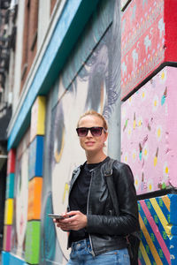 Young man wearing sunglasses standing against wall