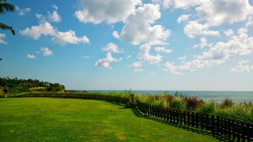 Scenic view of field by sea against sky