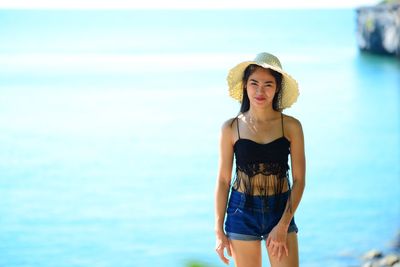 Young woman wearing hat standing at beach against sky