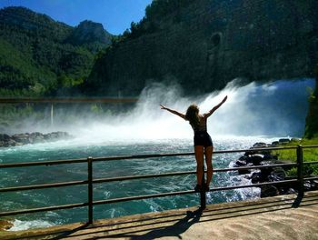 Rear view of woman standing on railing against waterfall