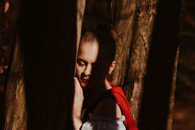 Close-up of young woman standing by tree trunk