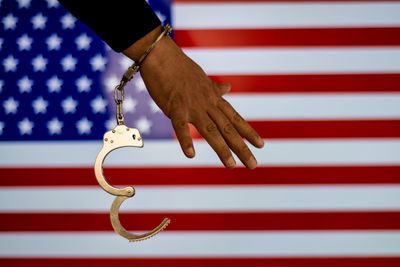 Cropped hand of male criminal with handcuffs against american flag