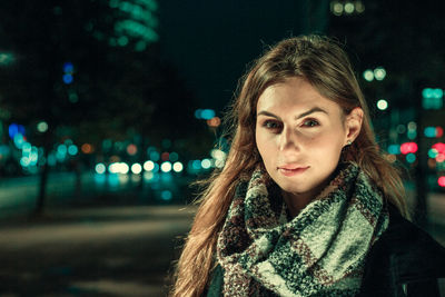 Portrait of young woman standing on street in city at night