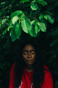 Young woman with eyes closed sitting against trees in park