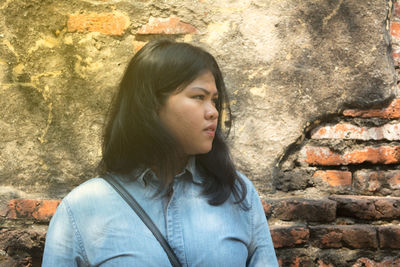 Young woman looking away against brick wall