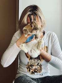 Young woman holding rabbit against face sitting at home
