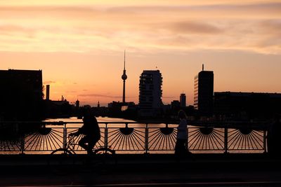 Silhouette fernsehturm and buildings by river against sky during sunset
