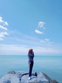 Woman looking at sea while standing on rocks against sky