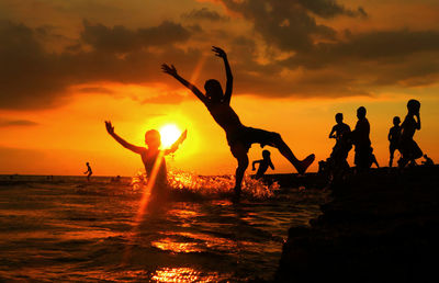 Silhouette people jumping on beach against sky during sunset