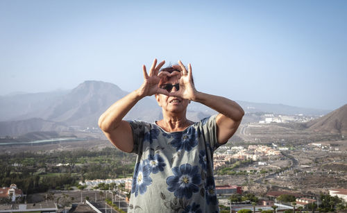 Woman making heart shape while standing on mountain