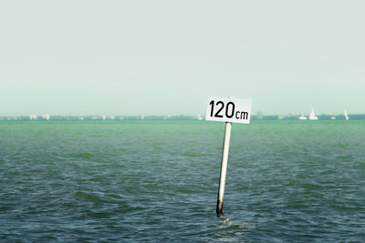 Information sign by sea against sky