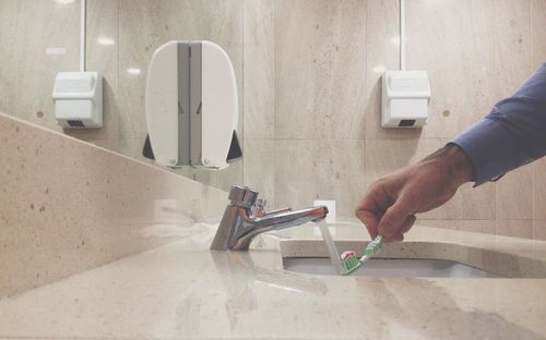 Cropped hand of man wetting toothpaste on toothbrush in bathroom