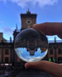 Cropped hand holding crystal ball against building in city