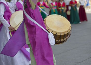 Women in traditional clothing with drums dancing on footpath in city