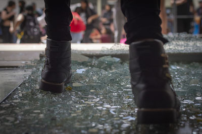 Low section of man standing on broken glass