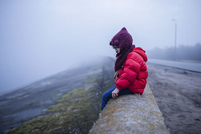 Rear view of woman on rock against sky during winter