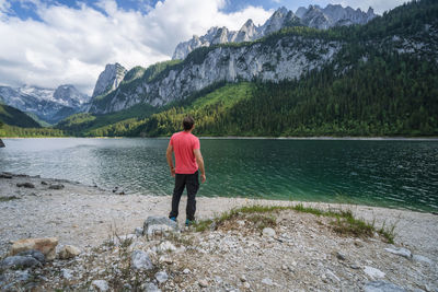 Rear view of man standing on mountain by lake