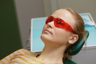 High angle view of woman wearing red eyeglasses while reclining on seat in clinic