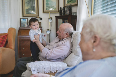 Happy baby girl standing with help of great-grandfather at home