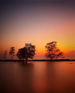 Silhouette trees by lake against romantic sky at sunset
