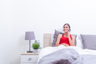 Young woman using mobile phone while sitting on bed at home