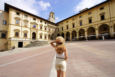Back view of young traveler woman in piazza grande square in the old town of arezzo, tuscany, italy.