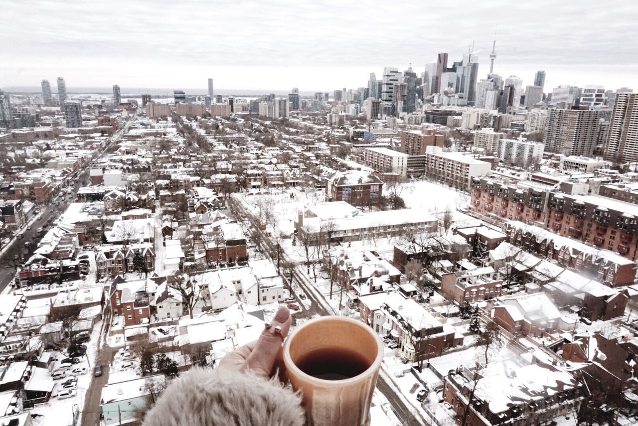 city, architecture, built structure, building exterior, snow, winter, cold temperature, real people, cityscape, human body part, human hand, one person, building, hand, food and drink, high angle view, drink, cup, outdoors