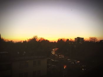 Silhouette trees and cityscape against sky during sunset