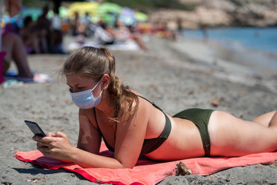 Woman wearing mask using mobile phone while lying on beach