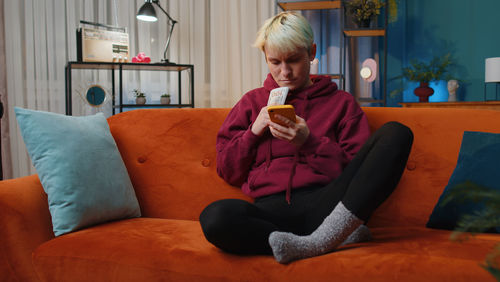 Young woman using phone while sitting on sofa at home